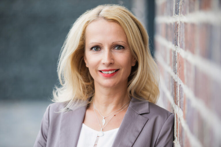 Eine Frau lehnt an einer Steinmauer für ihr Bewerbungsfoto in Dresden. natürliches Licht und diesen Hintergrund wirkt das Bild sehr modern, passend für ein sehr gute Bewerbungsfotos außerhalb eines Fotostudios.