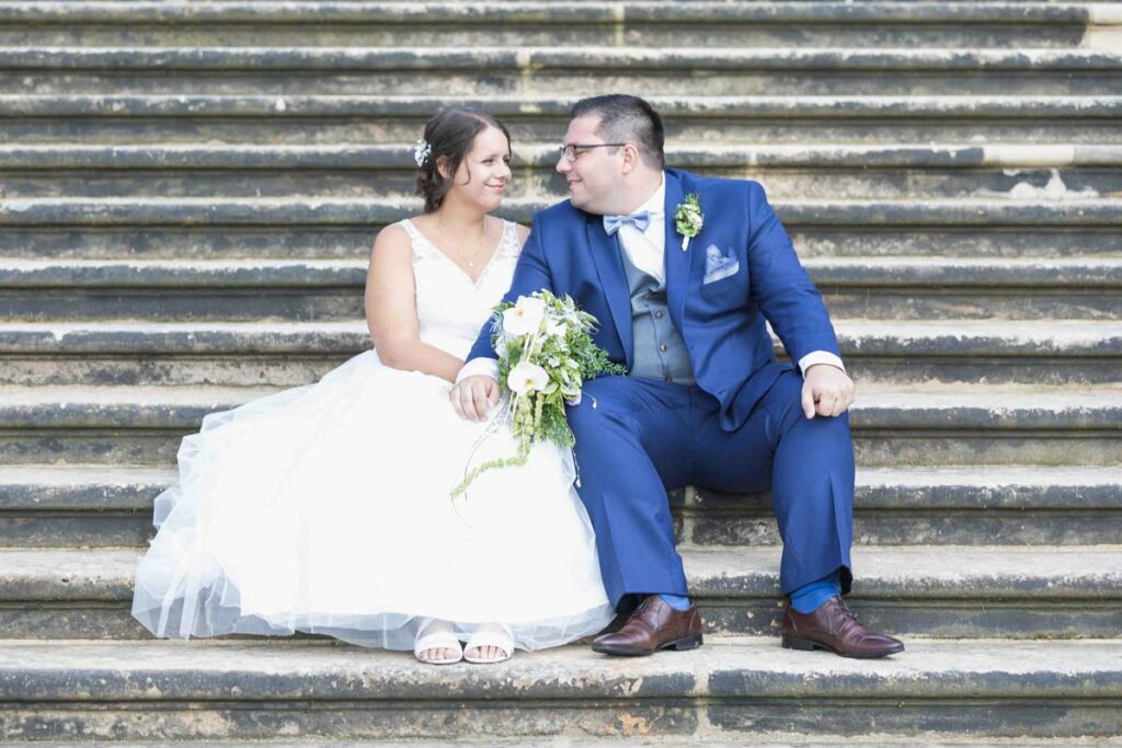 glückliches Ehepaar sitzt nebeneinander auf stufen in dem Barockgarten großsedlitz bei pirna