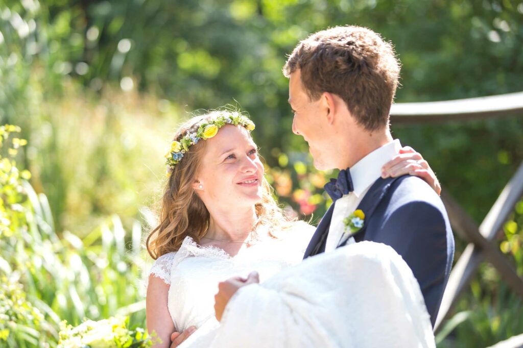 Die Braut wird auf Händen von Ihrem Mann getragen. Dabei schauen sie sich an und die Braut schaut sehr glücklich ihren mann an. Hochzeitsfotograf Freiberg - Jan Windisch Fotografie