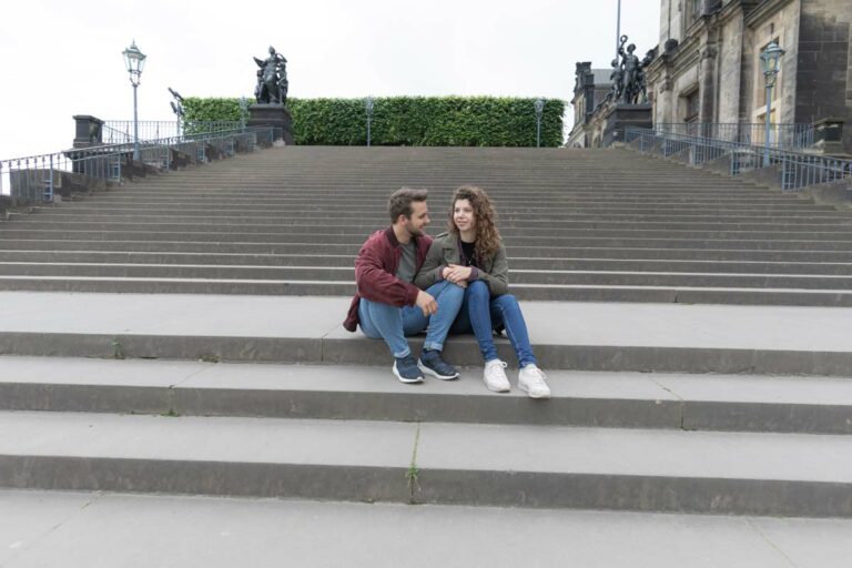 ein junges Paar sitzt in der Altstadt in Dresden auf einer Treppe und dabei umarmen sie sich liebevoll.