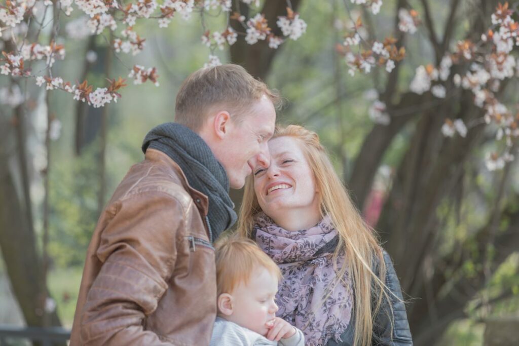 eine junge familie stehen nahe beisammen und die junge frau lächelt ihren mann an und der junge sitzt dabei in der mitte von seinen eltern... schöne Erinnerungen für die Ewigkeit. Natürliche und authentische Bilder.
