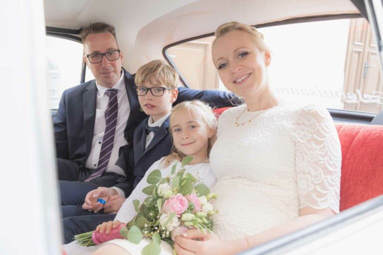 Brautpaar sitzt mit seinen Kindern in einem Auto und schauen in die Kamera - Hochzeitsfotografie görlitz