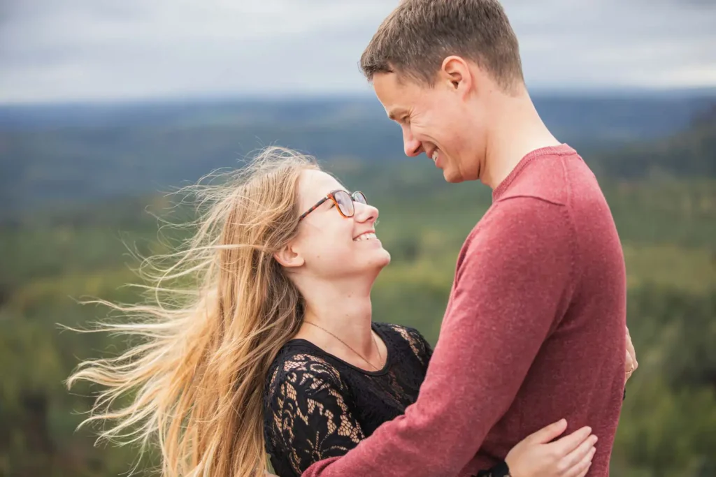 Paar umarmt sich und stehen zusammen und sind glücklich - im Hintergrund der Wald und die Berge - engagmentshooting dresden - sächsische Schweiz