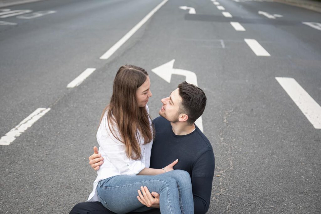 ein Paar sitzt auf einer Straße während eines Fotoshootings in Dresden und sie genießen die Zeit. Die Zuneigung zeigen sie auf den Fotos indem sie sich eng aneinander gekuschelt haben und sich umarmen.