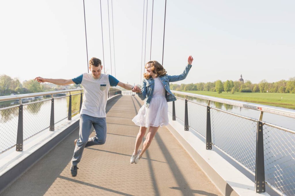 Fotoshooting auf einer Brücke eines jungen Paares in Dresden. Freude und Liebe sollen Bilder ausstrahlen und dafür benötigt man kein Fotostudio. Draußen entstehen die besten Aufnahmen. Das Paar springt hoch und freut sich , dabei schauen sie nicht in die Kamera des Fotografen.