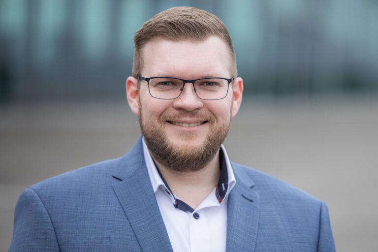 Mitarbeiter Porträt in Dresden vor einem natürlichen Hintergrund - Der Mann schaut in die Kamera des Fotografen und lächelt