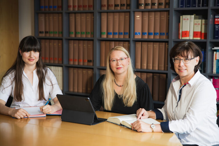 Mitarbeiterfotos bei der Arbeit. Die Frauen sitzen an einem großen Tisch und schauen in die Kamera des Fotografen.