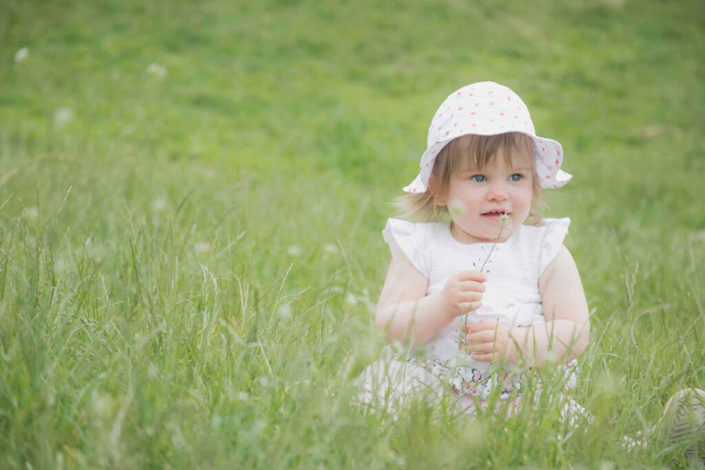 ein kleines Mädchen sitzt im Gras und hat eine Pusteblume gepflückt