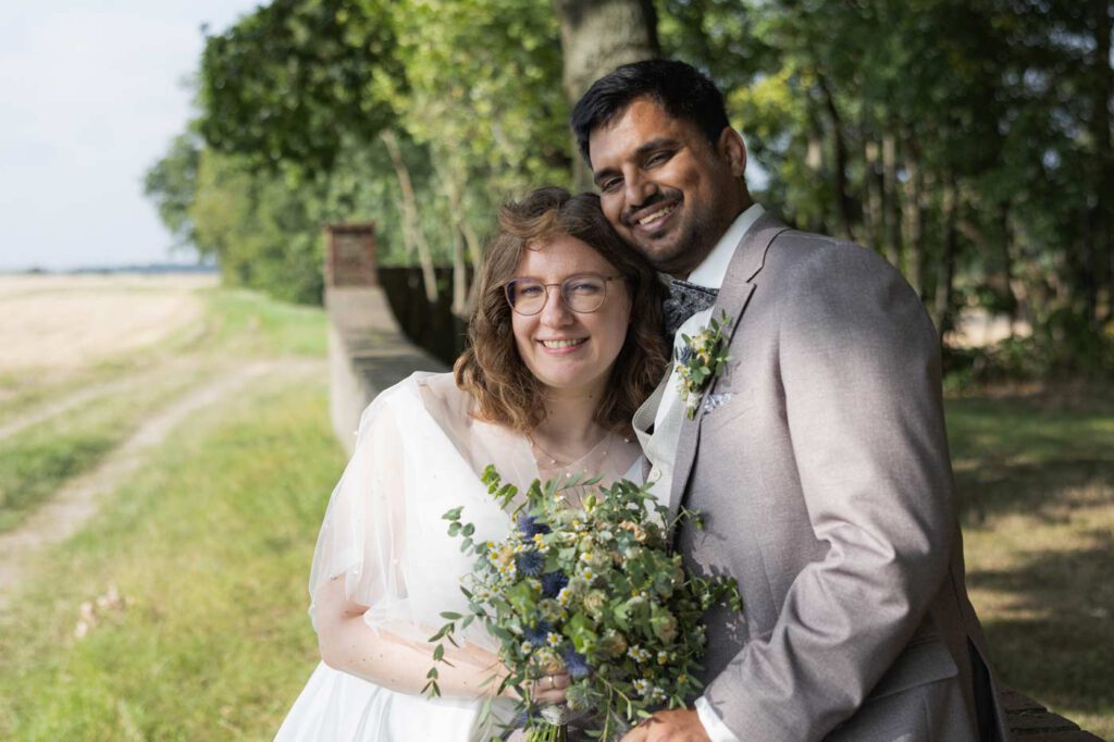 Bräutigam sitzt auf einer Mauer und seine Braut lehnt sich an ihn - Brautpaarshooting Hochzeit Bildungsgut Schmochtitz bei Bautzen