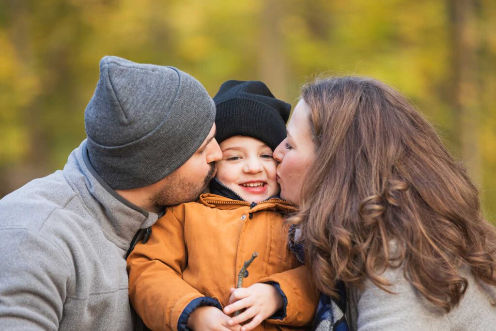 Fotoshooting im Herbst - Mama und Papa küssen ihr Kind