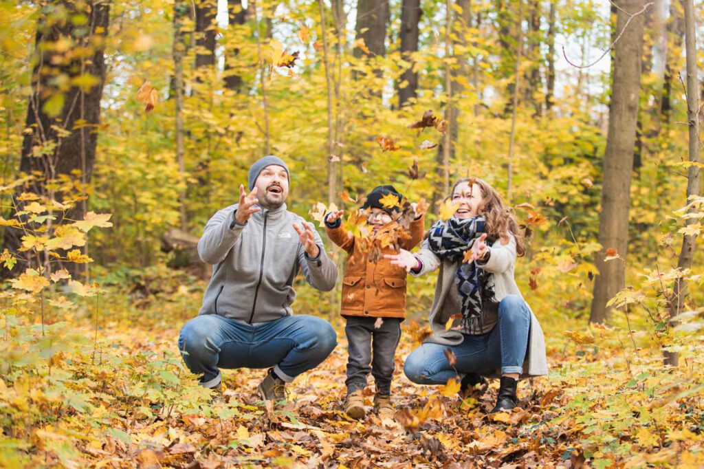 Familien fotoshooting im Herbst - Familie wirft Blätter hoch und freuen sich mit ihrem Kind