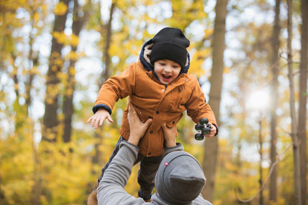 Papa wirft sein Kind hoch und im Hintergrund ist eine schöne Laubfärbung - Herbst Fotoshooting Dresden